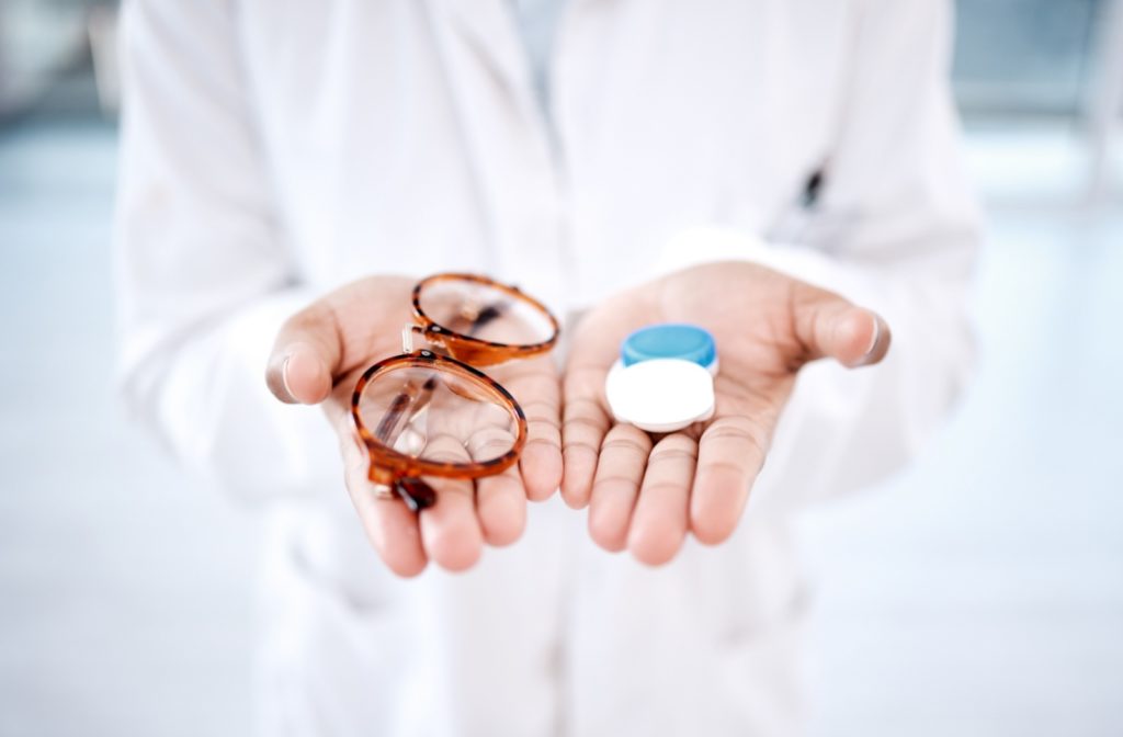 Optometrist holding glasses and contact lenses case in each hand.