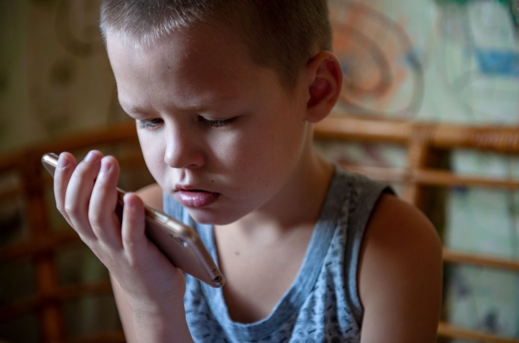 A close-up image of a child holding a phone very close to their face while watching something.