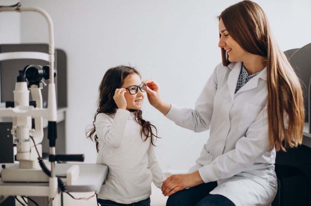 An eye doctor placing eyeglasses on a child's face to correct myopia.