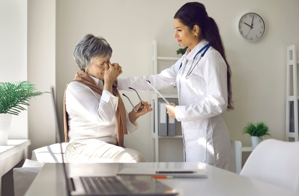 A senior pinches the bridge of their nose to alleviate eye pain while seeing an optometrist for help.