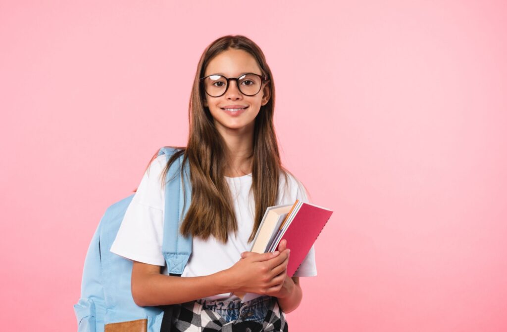 A cheerful child with a backpack and books wears myopia control eyeglasses to school.