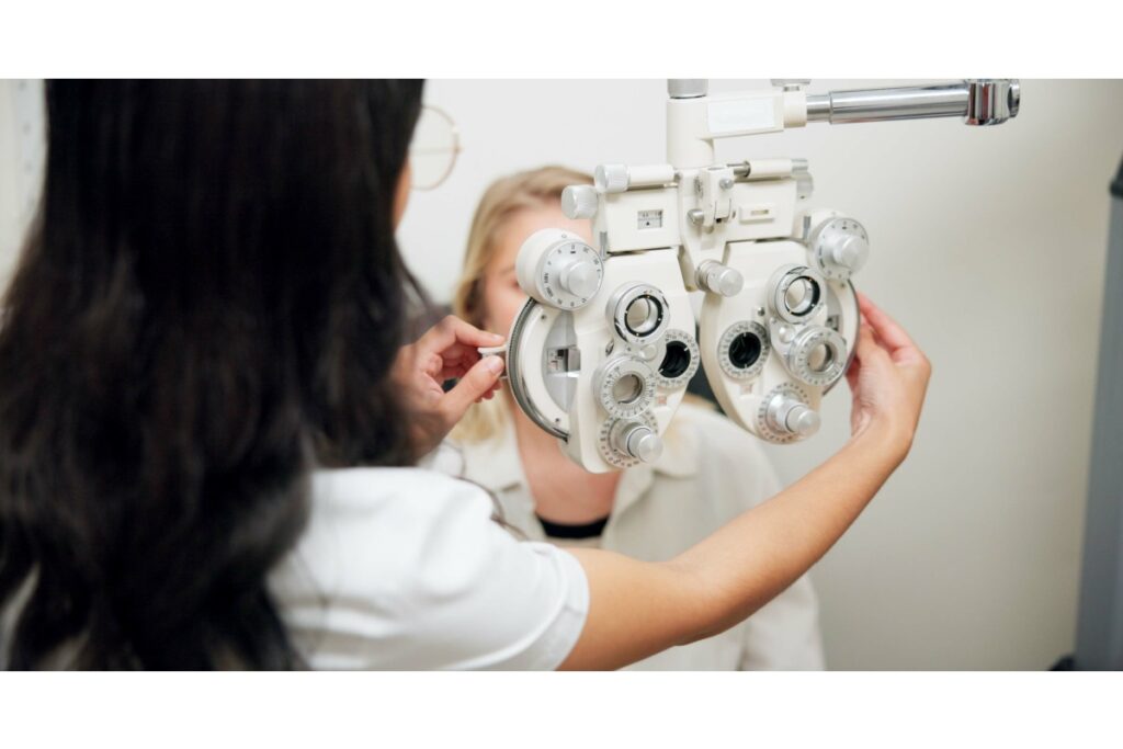 Optometrist adjusting a phoropter during an eye exam at Pinehouse Eyecare in Saskatoon. The patient looks through the instrument while the doctor fine-tunes lenses for precise vision testing.