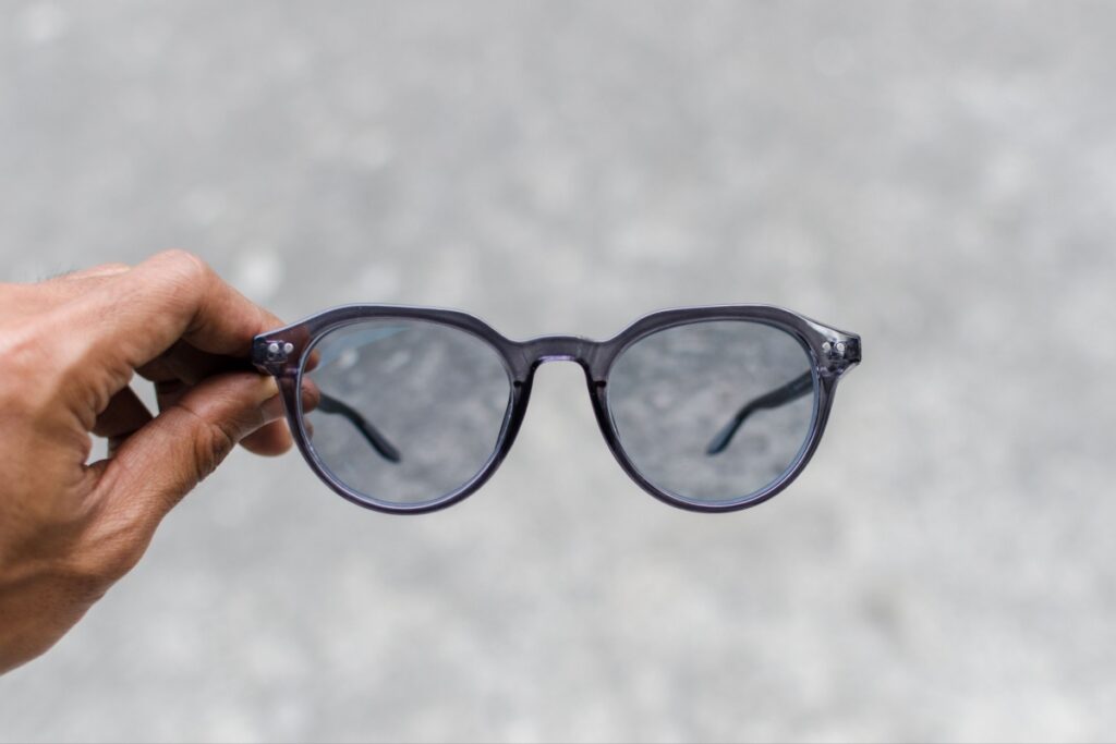 Person holding round navy blue frame eyeglasses with photochromic transition lenses showing partial tint activation against neutral background